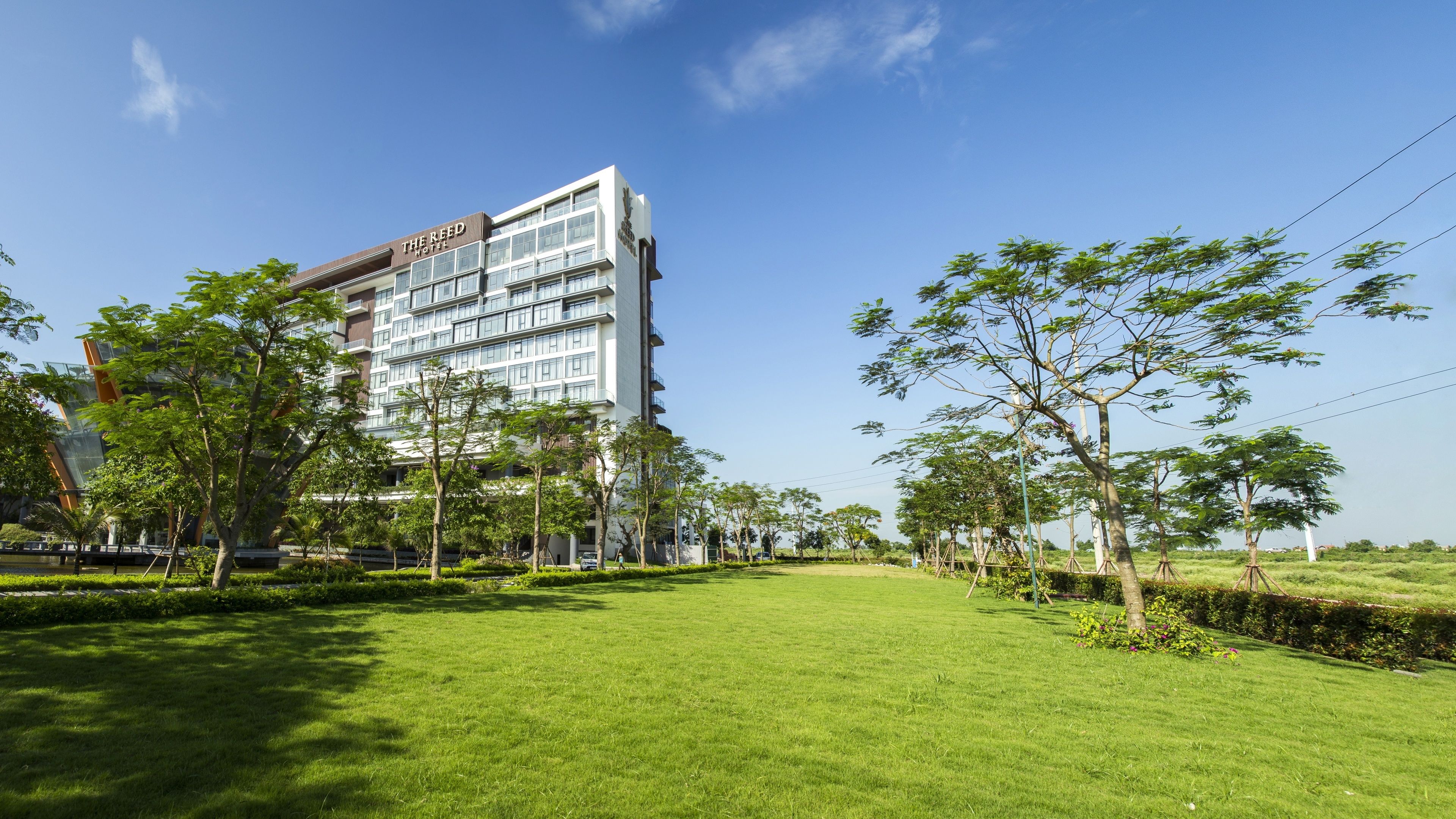 A modern hotel with a flat roof and multiple floors, surrounded by well-maintained grass and trees.
