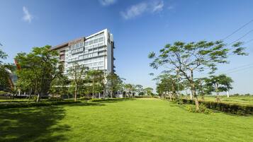 A modern hotel with a flat roof and multiple floors, surrounded by well-maintained grass and trees.