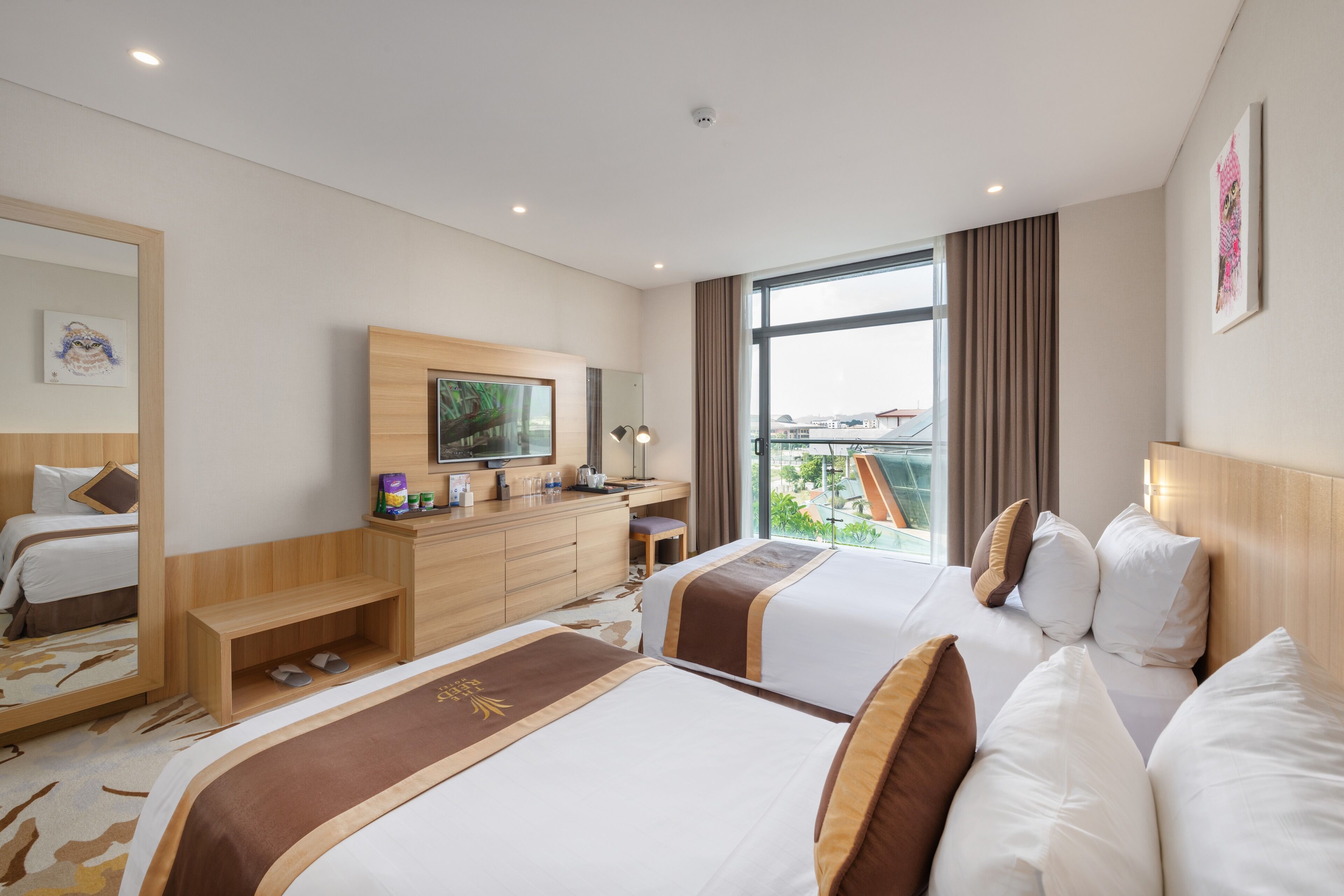 A hotel room with two beds, a desk, a television, and a large window with a view.