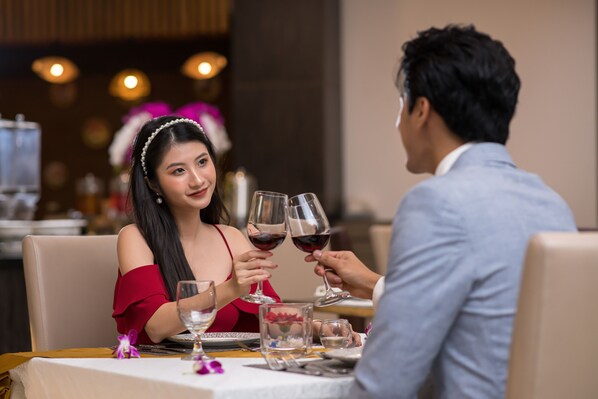 A couple seated at a table with wine glasses, a dessert plate, and a vase with flowers.