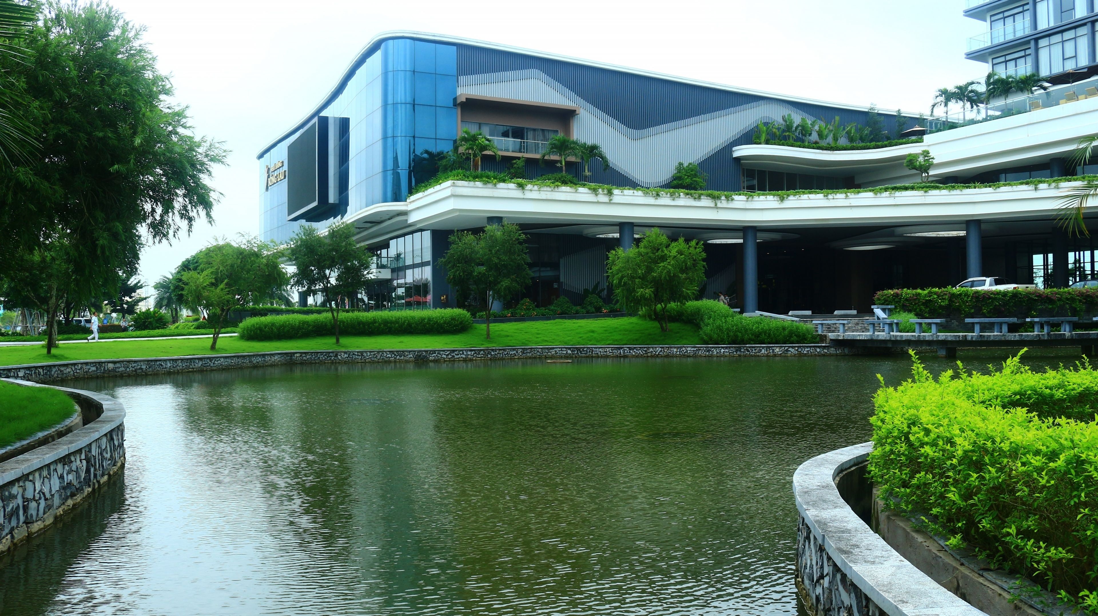 Un edificio moderno con fachada curva, jardín ajardinado y fuente de agua.