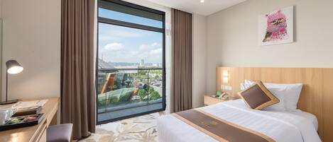 Habitación de hotel con un amplio ventanal, una cama con cabecera marrón, un escritorio con lámpara y vistas a la ciudad.
