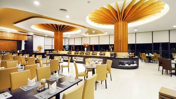 A modern restaurant with a central bar, multiple dining tables, and a high ceiling with unique wooden light fixtures.