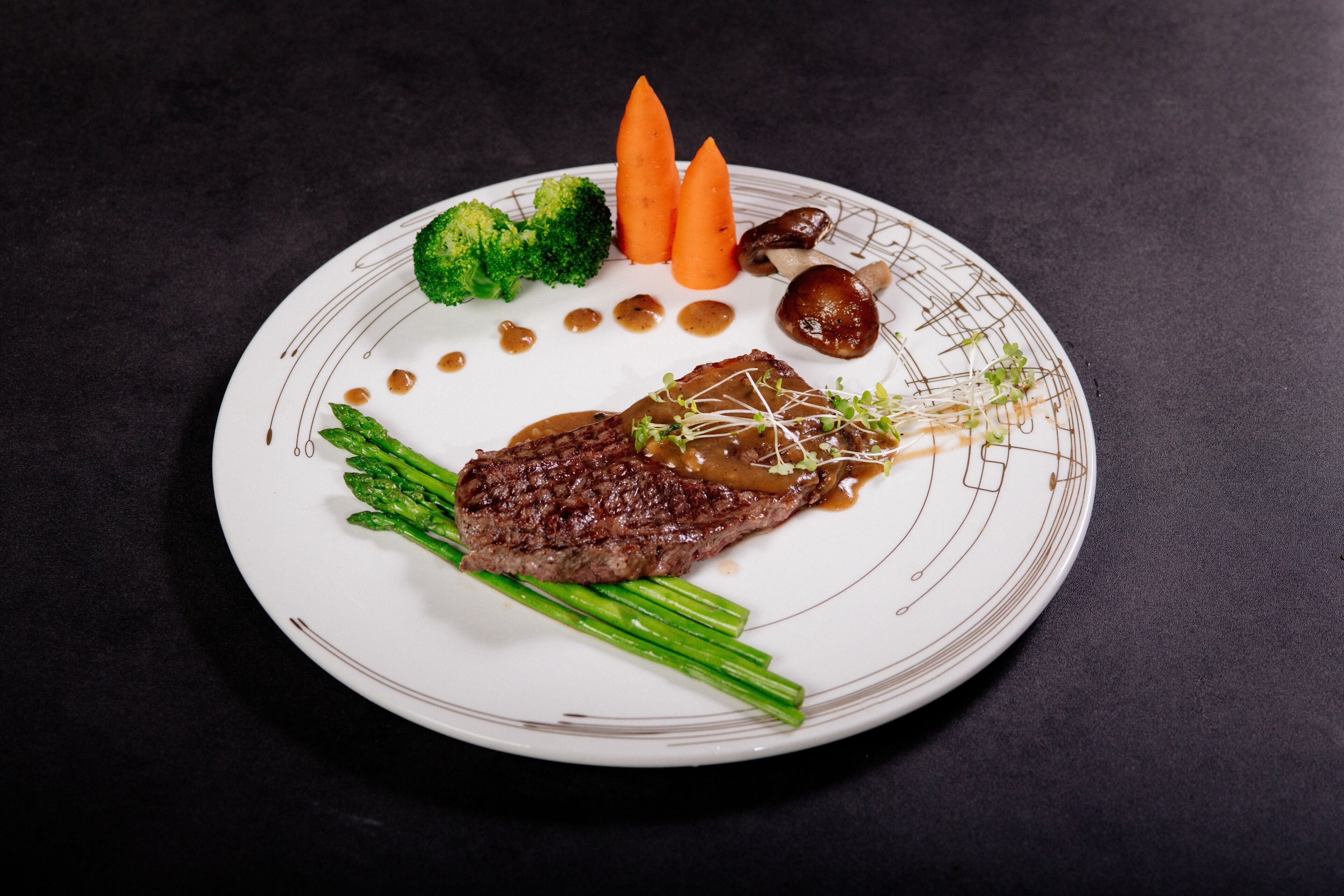 Un plato con un bistec, espárragos, zanahorias y champiñones.