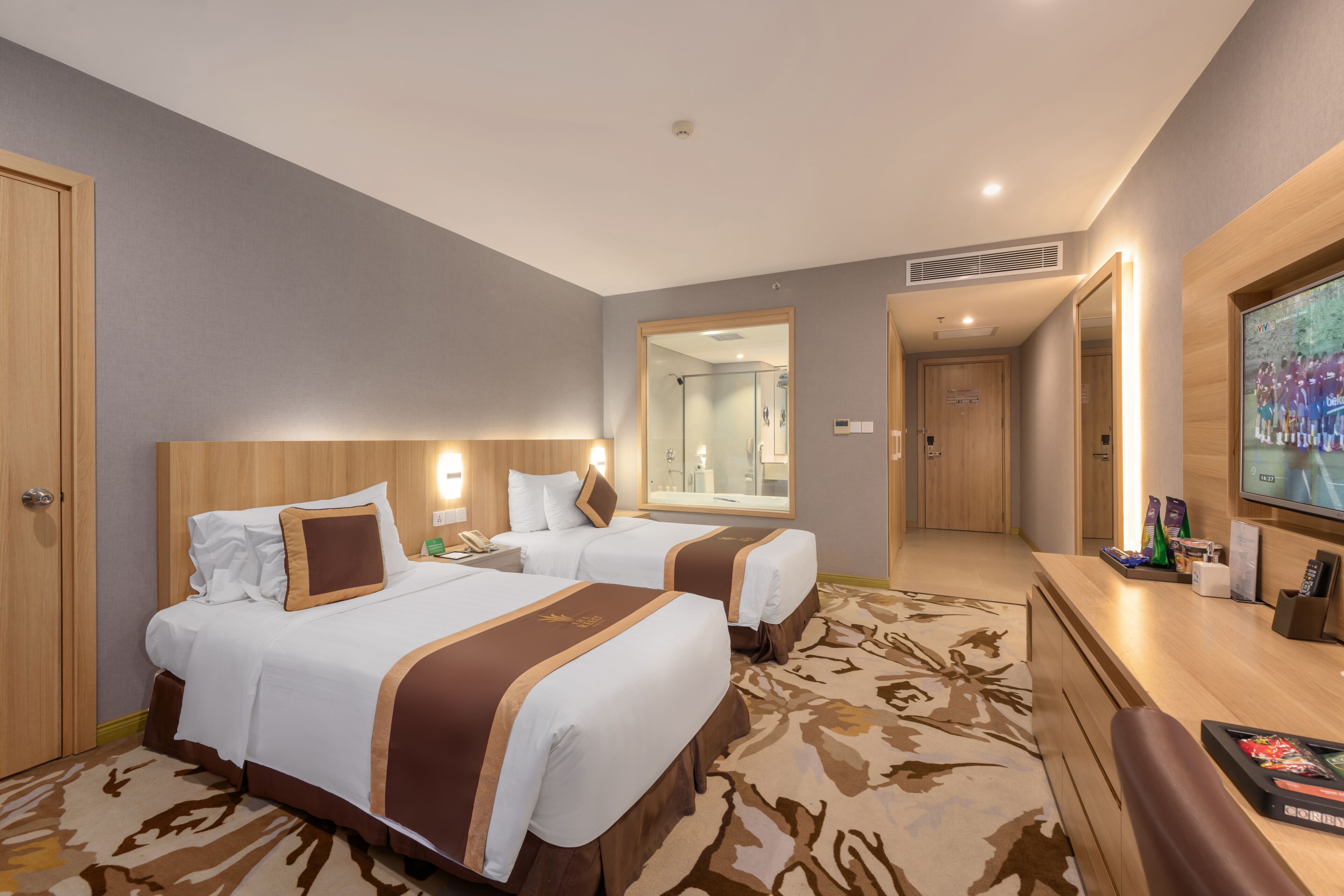A hotel room with two beds, a television, a mirror, a bathroom, and a carpeted floor.