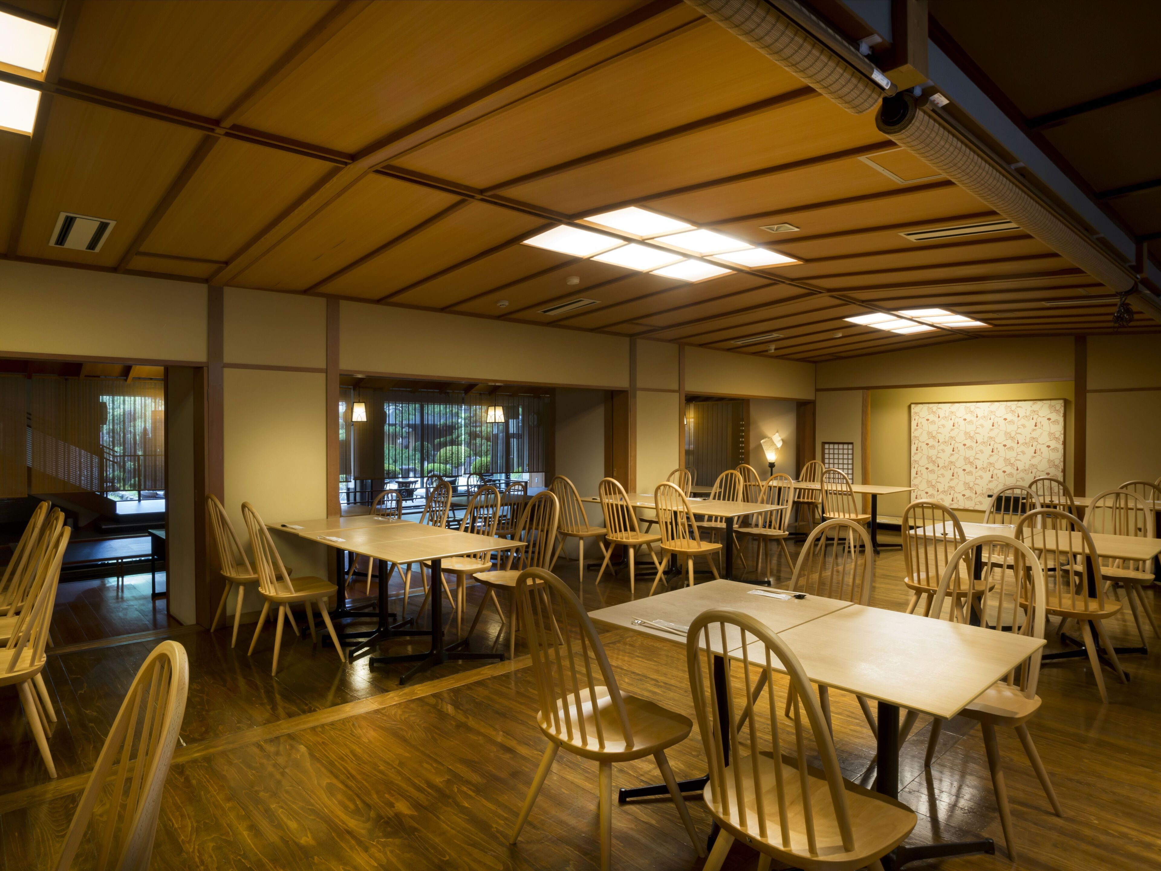 Un salón de conferencias con varias mesas y sillas, suelo de madera y un techo alto con vigas a la vista.