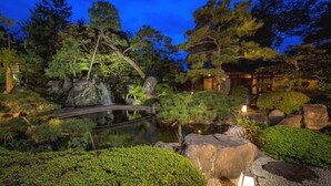 A traditional Japanese garden at dusk with a pond, rocks, and a bridge. - Hotel Yagi (Awara)