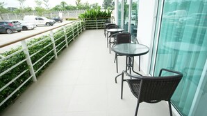 A balcony with outdoor seating, a white railing, and a view of parked cars and greenery. - Donchan Residence (Chiang Mai)
