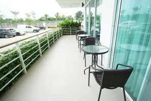 A balcony with outdoor seating, a white railing, and a view of parked cars and greenery. - Donchan Residence (Chiang Mai)