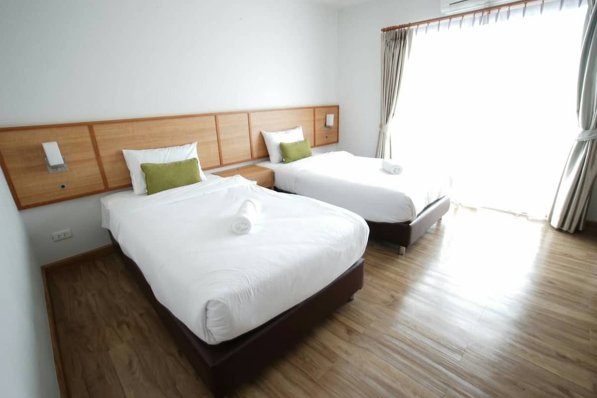 A hotel room with two beds, wooden headboards, white bedding, and a large window with curtains.