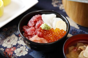A bowl of assorted food items including fish, roe, and other delicacies, placed on a table with a floral pattern.