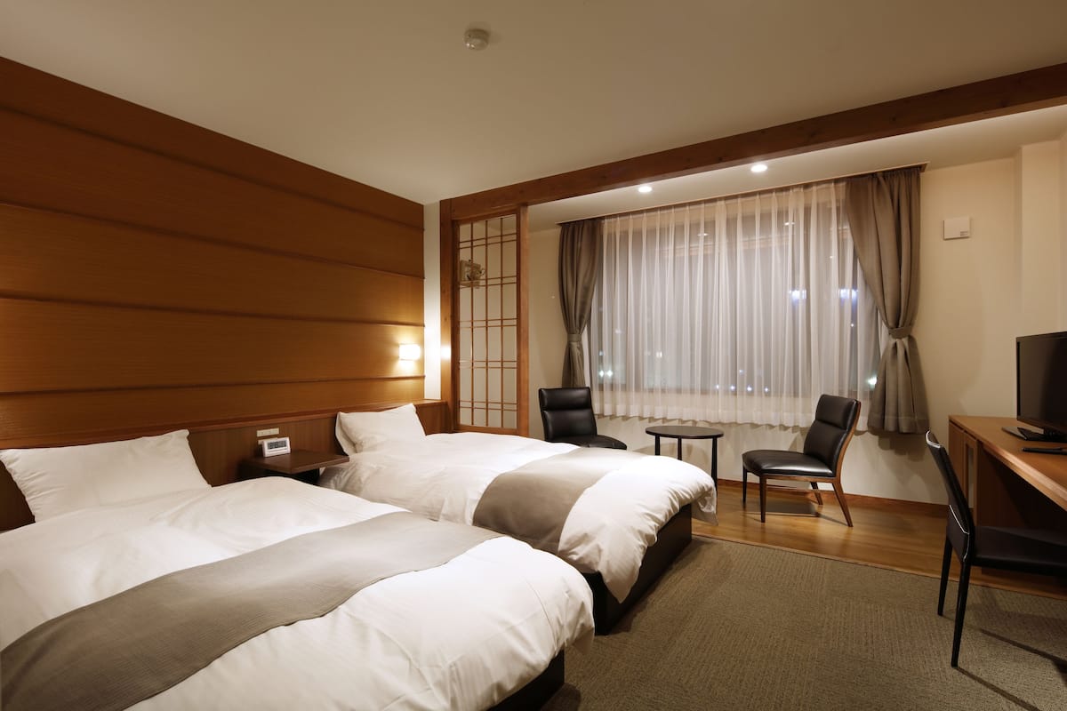 Une chambre d’hôtel avec deux lits, un bureau, une chaise et un téléviseur.