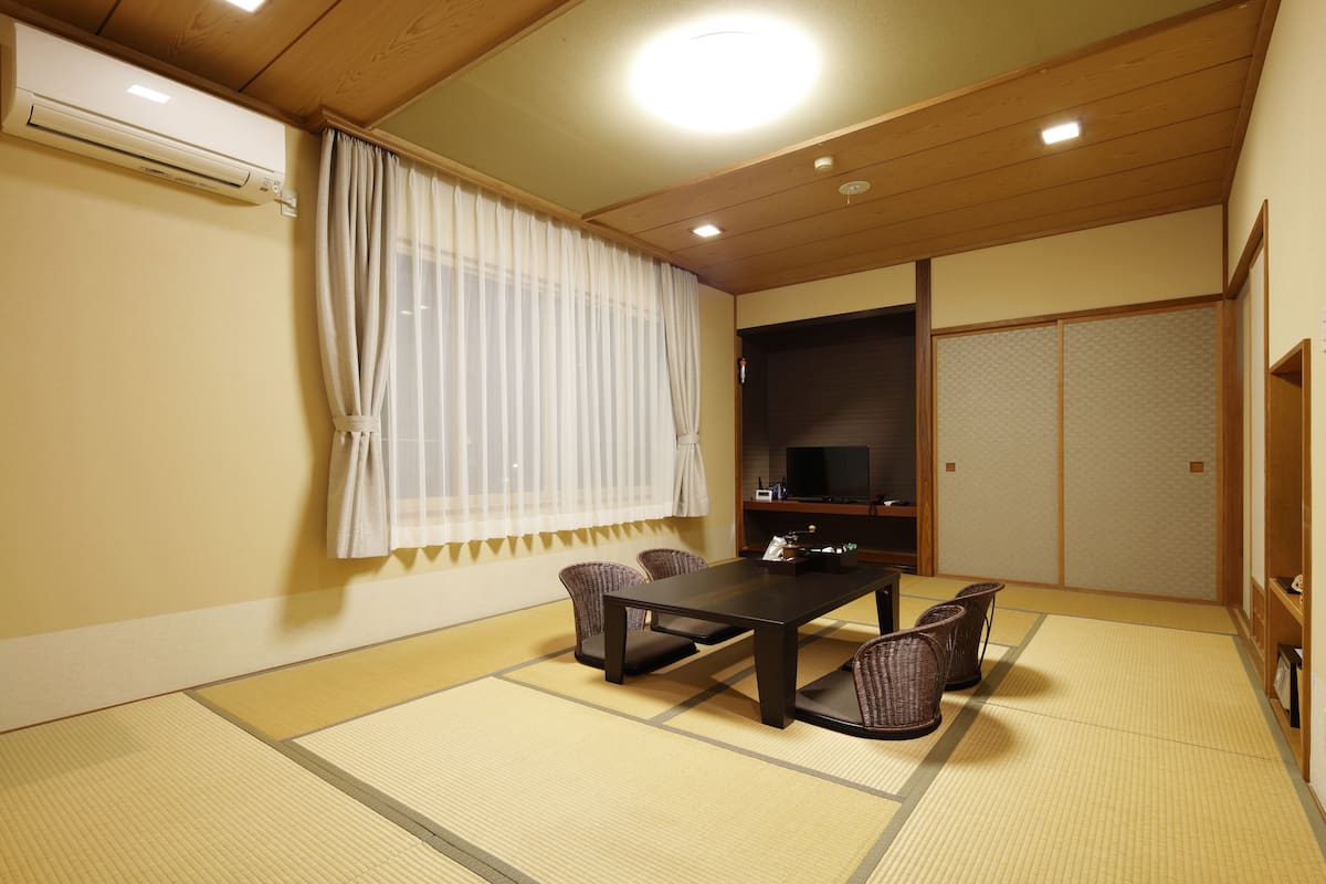 Une pièce de style japonais traditionnel, avec un sol recouvert de tatamis, une table basse et quatre chaises.