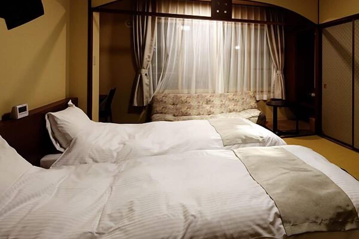 Une chambre d’hôtel avec deux lits, un plafond en bois, une horloge fixée au mur et une fenêtre avec des rideaux.