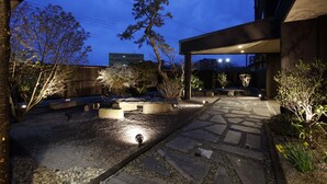 A well-lit outdoor area with stone pathways, seating arrangements, and a variety of plants. - Yunokawa Onsen Emi Hakodateya (Hakodate)