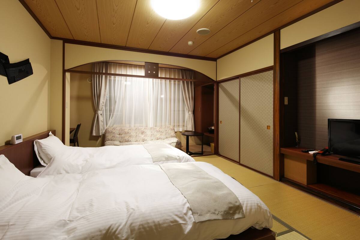 Une chambre d’hôtel équipée d’un lit, d’une télévision et d’une porte coulissante de style japonais traditionnel.