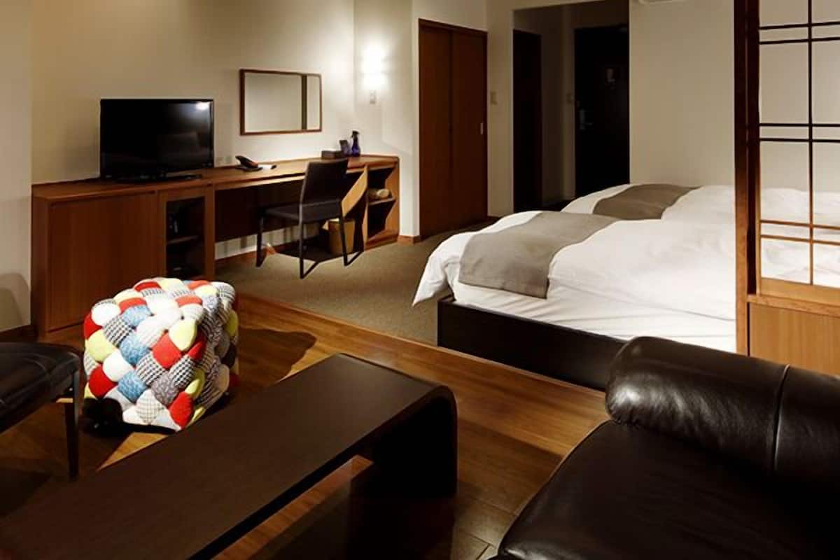 Une chambre d’hôtel comprenant un lit, un bureau avec un ordinateur, une télévision et un coin salon avec un coussin.