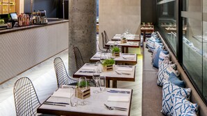 A modern restaurant with high ceilings, exposed concrete pillars, and a long dining area with cushioned seating.
