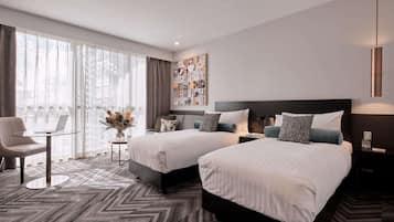 Habitación de hotel con dos camas, un escritorio y un ventanal grande.