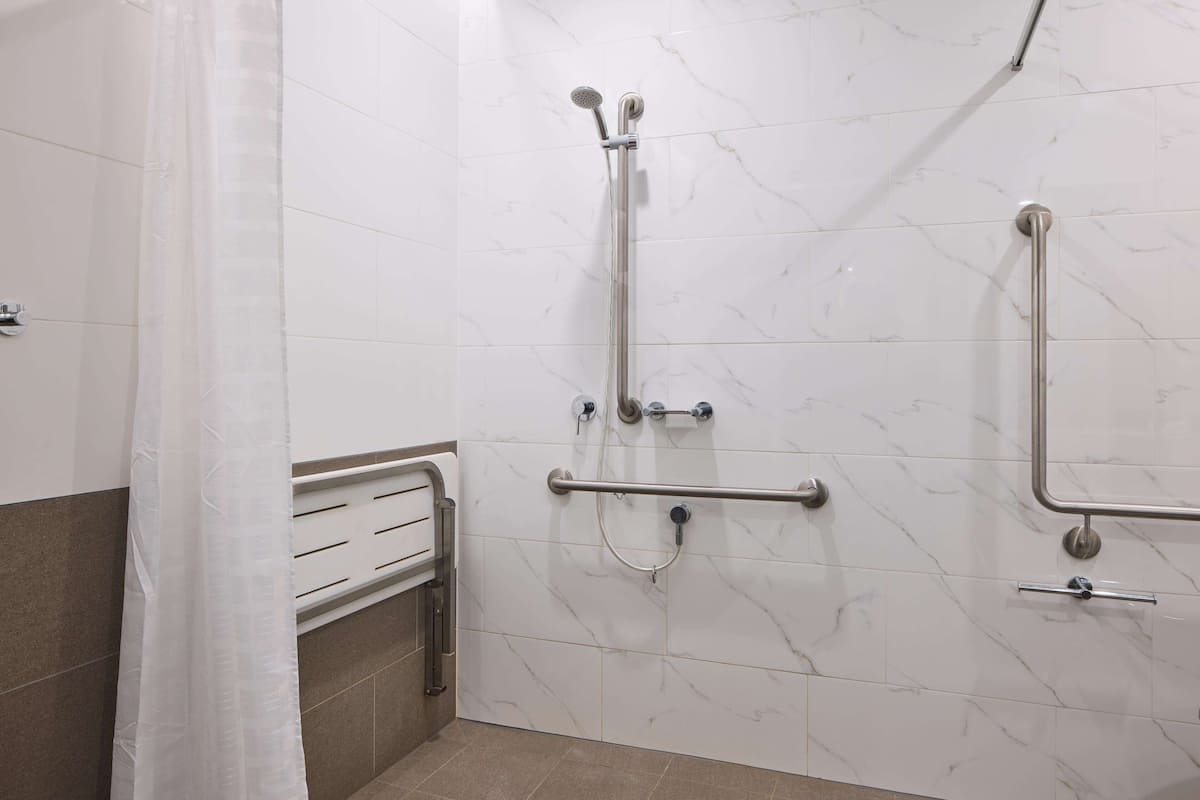 A bathroom with white marble walls, a shower with grab bars, and a towel rack.