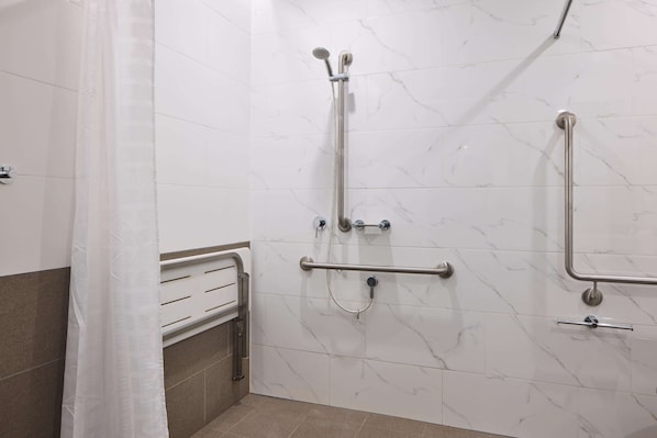 Un baño con paredes de mármol blanco, ducha con barras de apoyo y toallero.