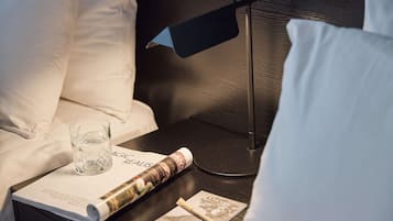 A neatly made bed with white linens, a glass of water, a magazine, and a small card on the nightstand.