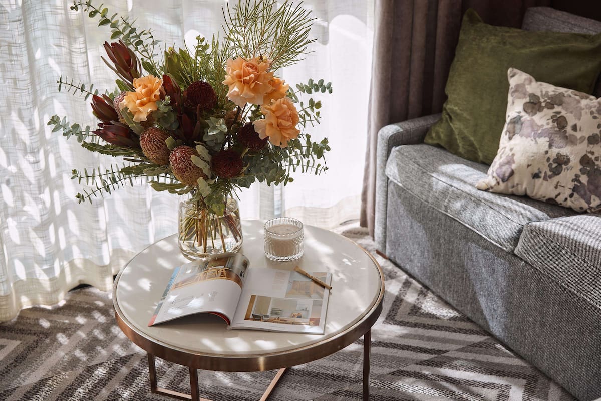 A round glass table with a magazine, a candle, and a floral arrangement.