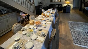 Ein Essbereich mit einem langen Tisch, der für eine Mahlzeit gedeckt ist, einer Treppe, die in ein Obergeschoss führt, und Blick ins Freie.