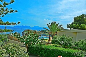 A coastal view with a pool, mountains in the background, and lush greenery.