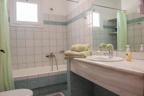 A bathroom with a bathtub, a sink, a mirror, and a window.