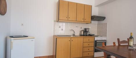 A compact kitchen with wooden cabinets, a white refrigerator, a stove, and a dining table.