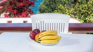 Ett bord med en fruktskål, en stol och utsikt över havet och ett träd.