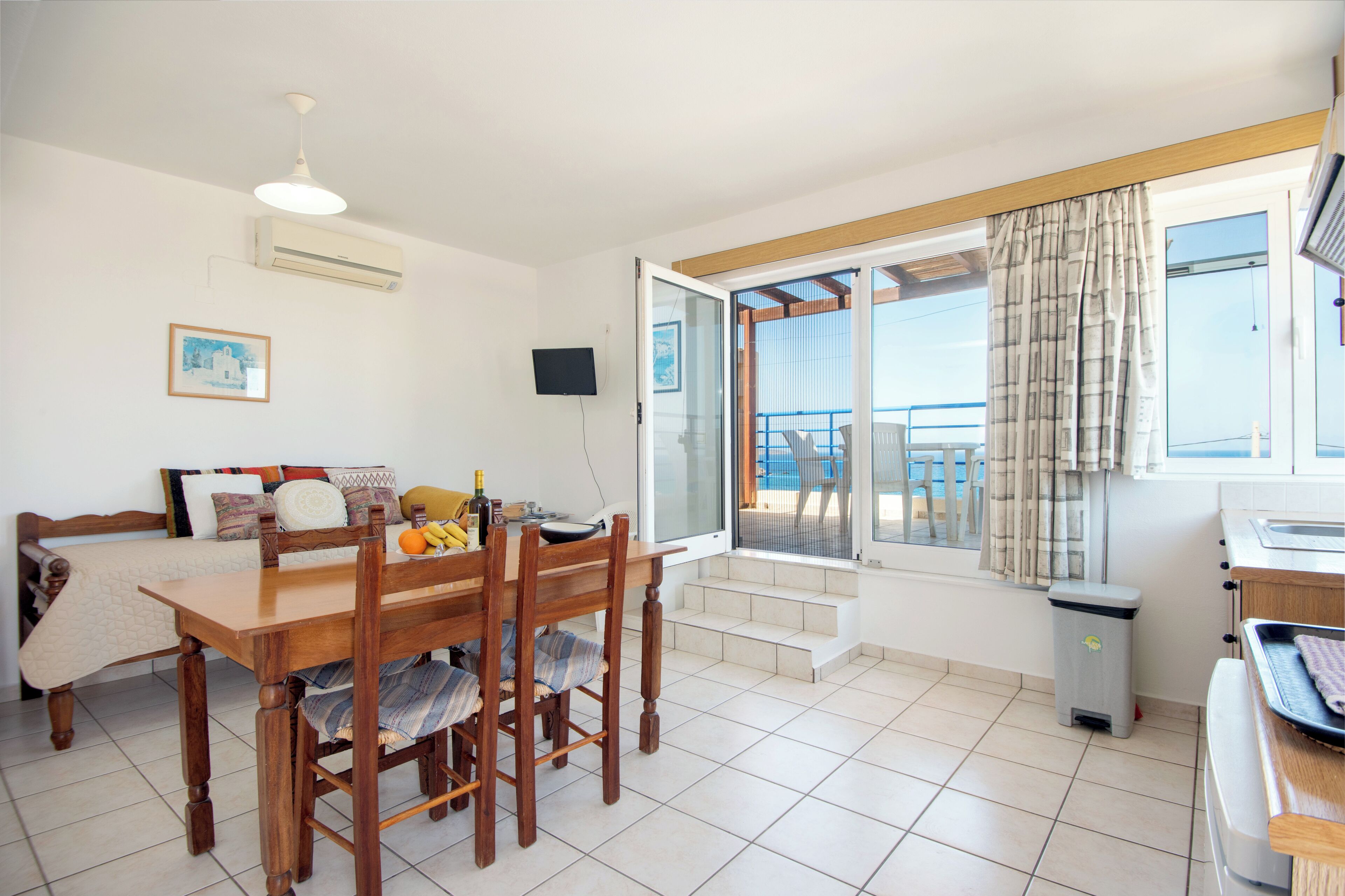 A room with a dining table, chairs, a sofa, a TV, an air conditioner, a window with curtains, and a balcony.