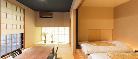 A traditional Japanese-style room with tatami flooring, a low wooden table, and two beds with white bedding.
