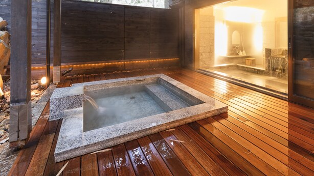 A hot tub in a wooden deck area with a view of a bathroom through a glass door. - Yushintei (Hakone)