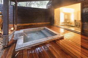 A hot tub in a wooden deck area with a view of a bathroom through a glass door.
