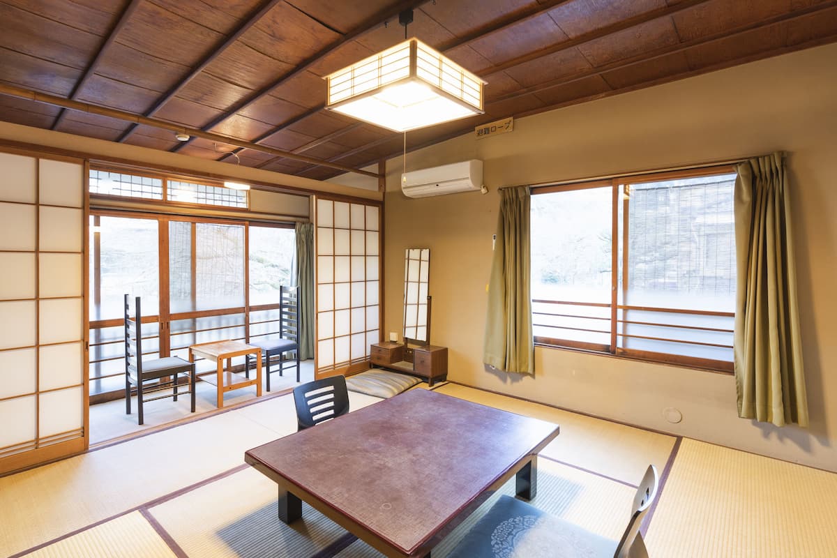 A traditional Japanese room with tatami flooring, a low table, chairs, and sliding doors.