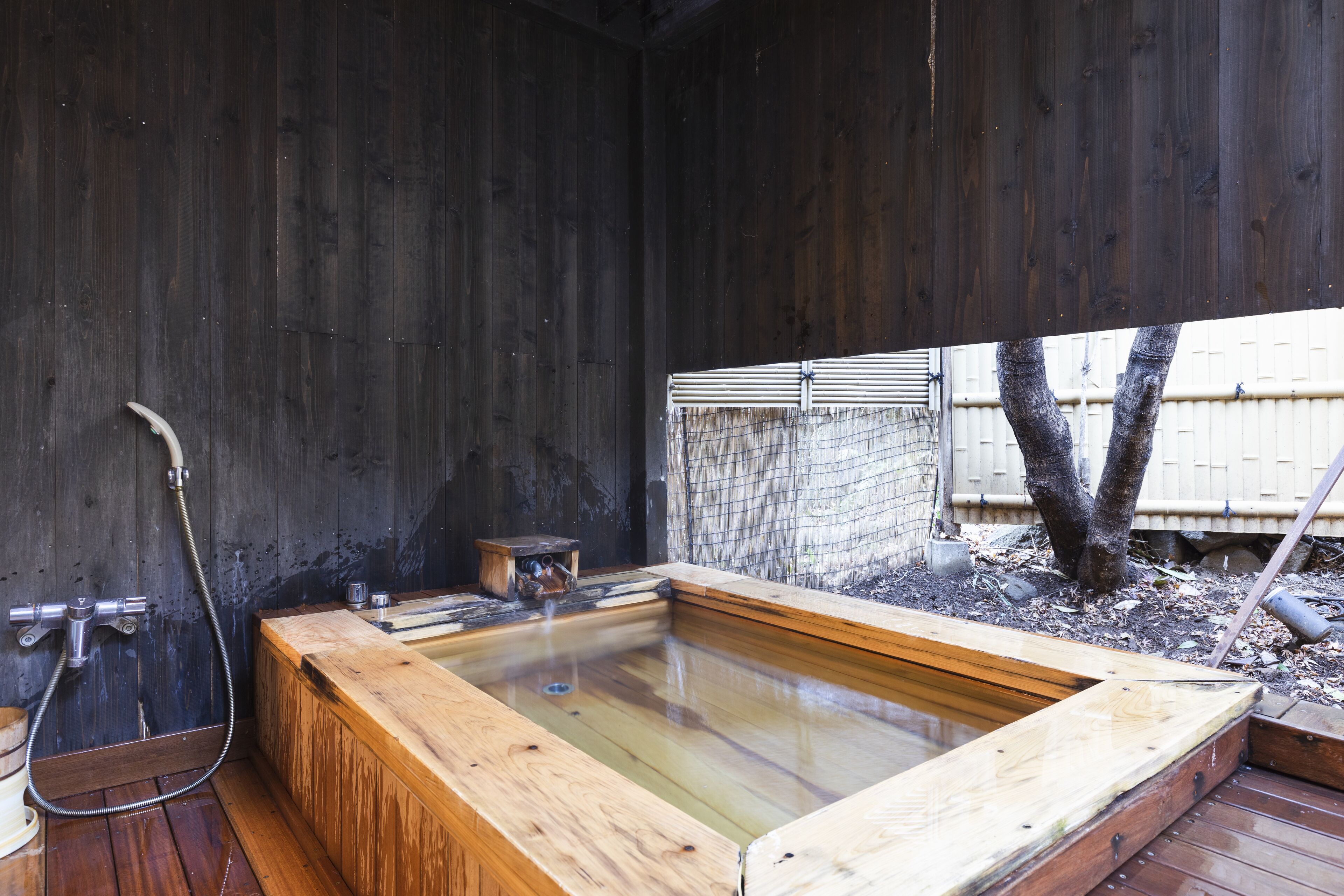 Una bañera de hidromasaje de madera con una terraza de madera, un taburete de madera y una manguera.