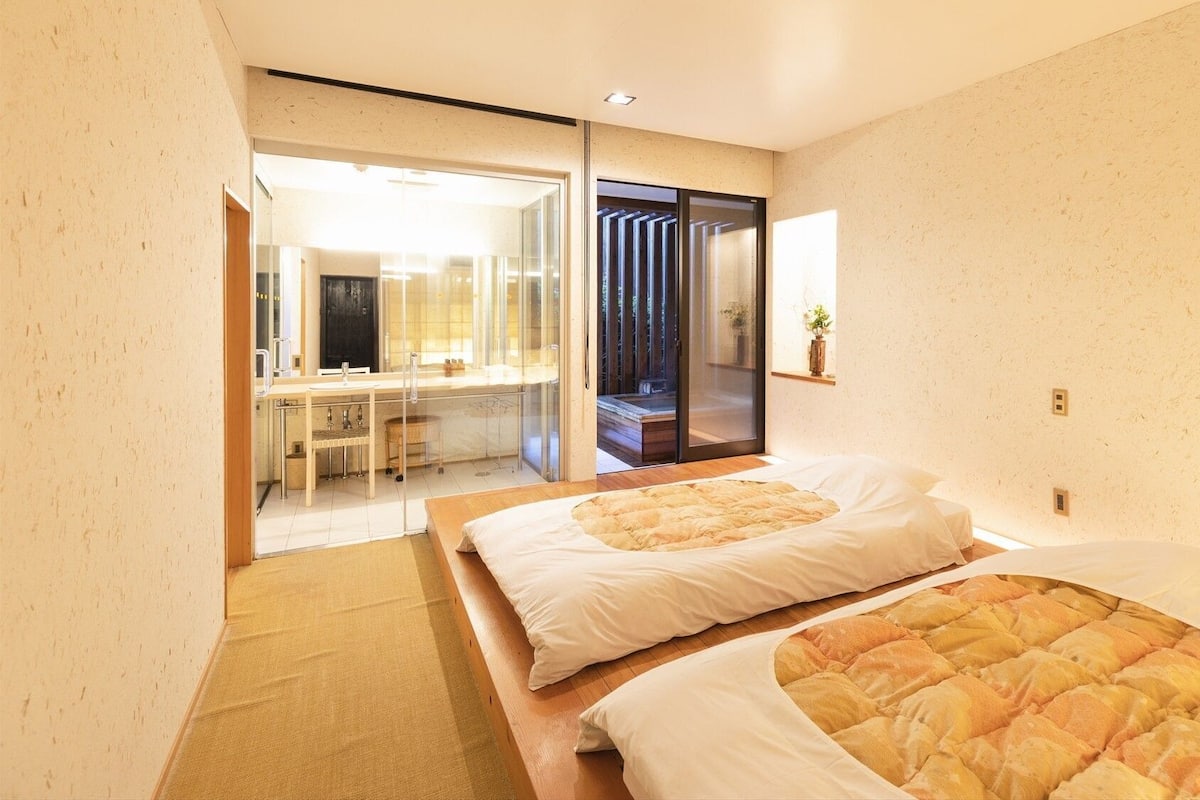 A hotel room with two beds, a sitting area with a table and chairs, and a sliding glass door leading to a balcony.