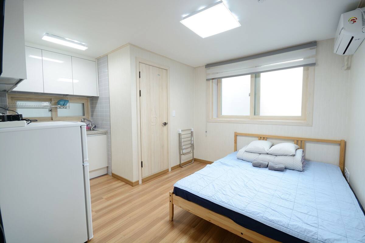 Un dormitorio con cama, ventana, armario y una zona de cocina.