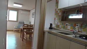 Une cuisine compacte avec un plan de travail carrelé, un évier et une cuisinière. On aperçoit à l’arrière-plan un coin repas avec une table et des chaises.