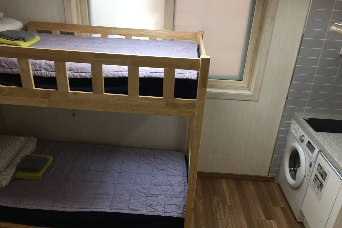 Una cama individual superpuesta con lavadora y ventana en la habitación.