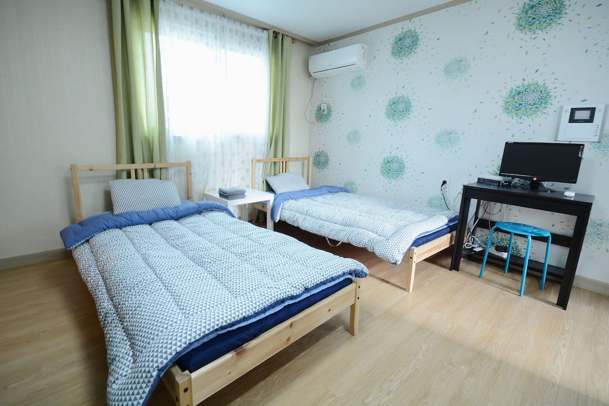 Una habitación con dos camas de madera, un escritorio, una silla y un televisor.