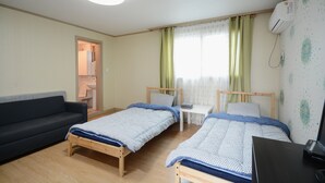 Une pièce avec deux lits en bois, un canapé sombre, une petite table blanche et un bureau avec un ordinateur.