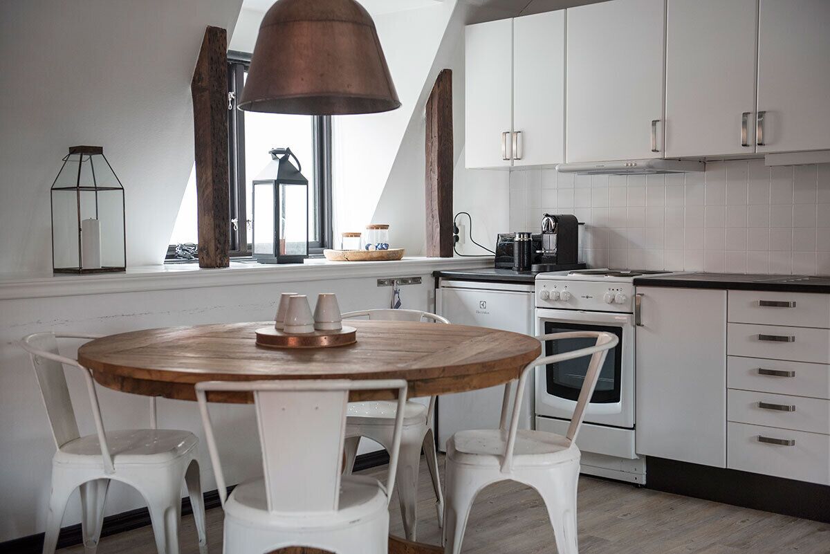 Una cocina moderna con armarios blancos, una mesa redonda de madera y sillas blancas.