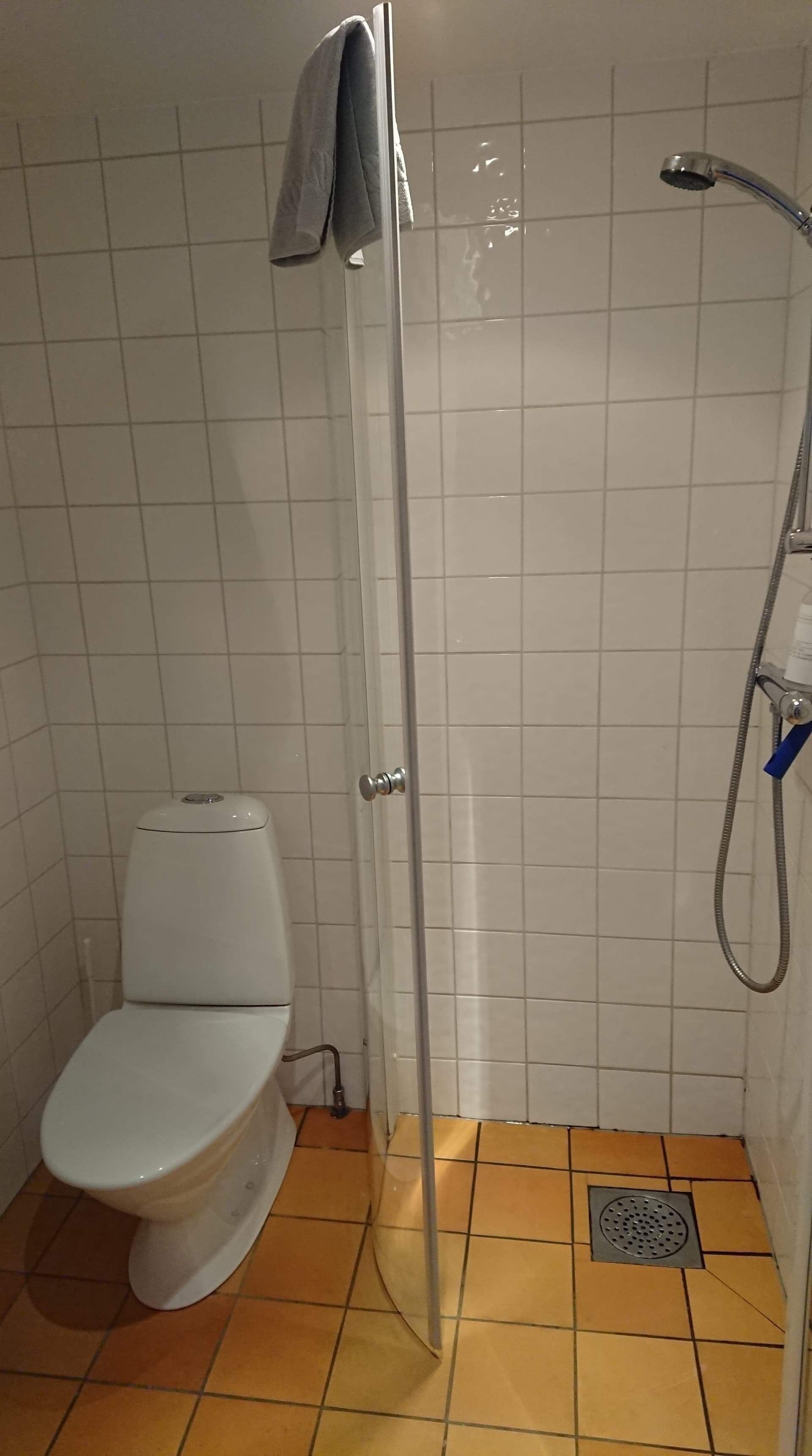 Un baño pequeño con inodoro, ducha y suelo de baldosas.