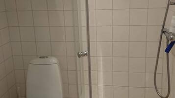 Un baño pequeño con inodoro, ducha y suelo de baldosas.