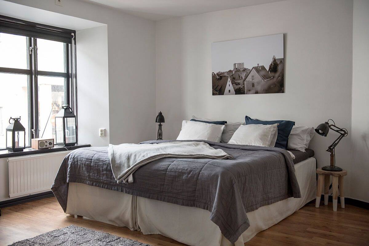 A bedroom with a large bed, a window with a view, a radiator, and a small table with a lamp.