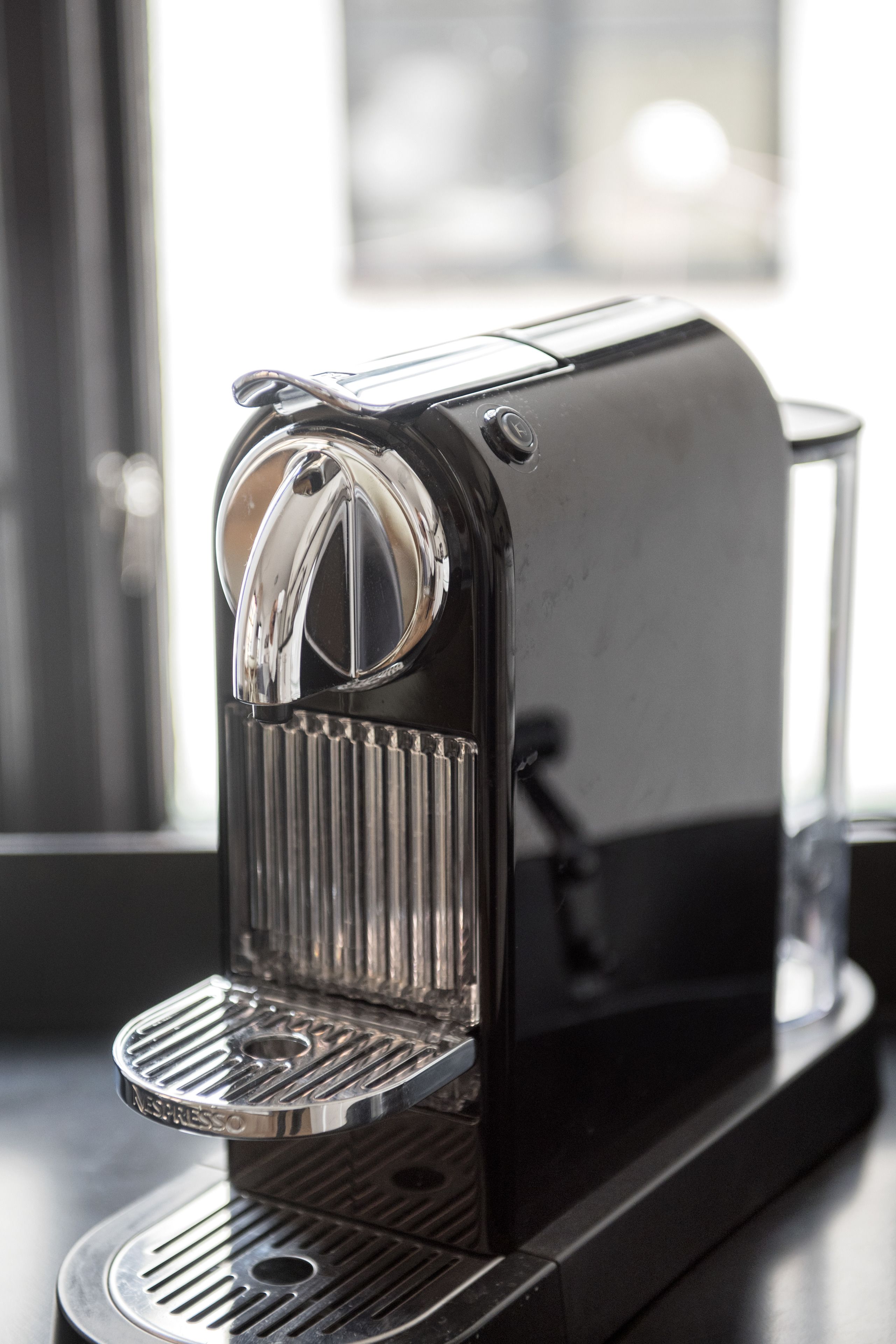 Une machine à expresso noire dotée d’un réservoir d’eau transparent et d’un bac de récupération en métal.