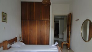 A bedroom with two single beds, a wooden wardrobe, a mirror, and a small table with a lamp. - Paradise Inn (Agios Nikolaos)